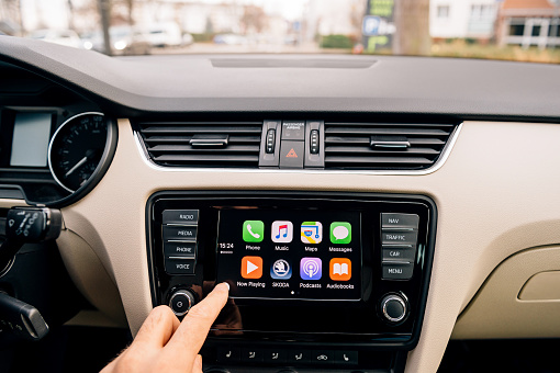 Paris, France - December 13, 2016: Man pressing home button on the Apple CarPlay main screen in modern car dashboard. CarPlay is an Apple standard that enables a car radio or head unit to be a display and controller for an iPhone. It is available on all iPhone 5 and later with at least iOS 7.1.