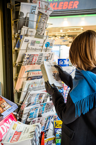 Paris, France - January 21, 2017: Woman purchases a The Wall Street Journal US newspaper from a newsstand featuring headlines with Donald Trump inauguration as the 45th President of the United States in Washington, D.C