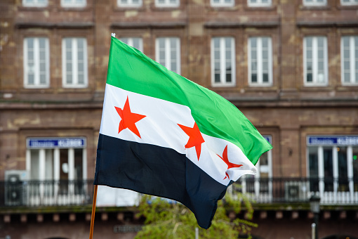 National flag of Syria waving during protest with European architecture in the background