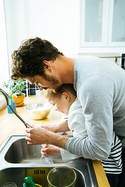 Father Washing Sons Hands In Kitchen Sink After Cooking Together