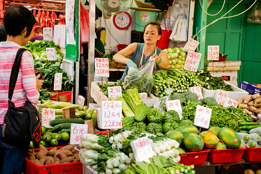 Hong Kong, China - October 28, 2016: Shopping street at Sau Kei Wan Market, China. Woman working at market stall, selling vegetable.
