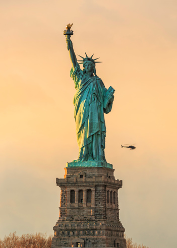 Front view of the Statue of Liberty with a helicopter that surrounds it. Taken during a beautiful sunset.
