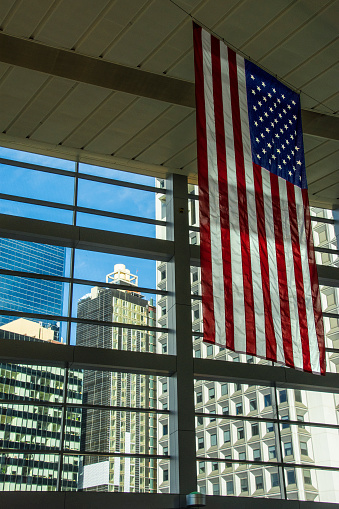 American flag hanging inside a building with a view of Lower Manhattan out the windows. New York City, New York.