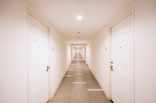 Corridor inside white building in orange tone lamp. Position of room doors are opposite alongside the way.