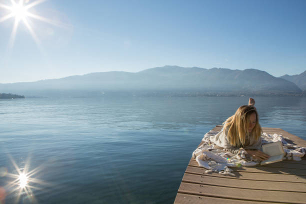 istock One young woman lying down on lake pier, reading book 639892590