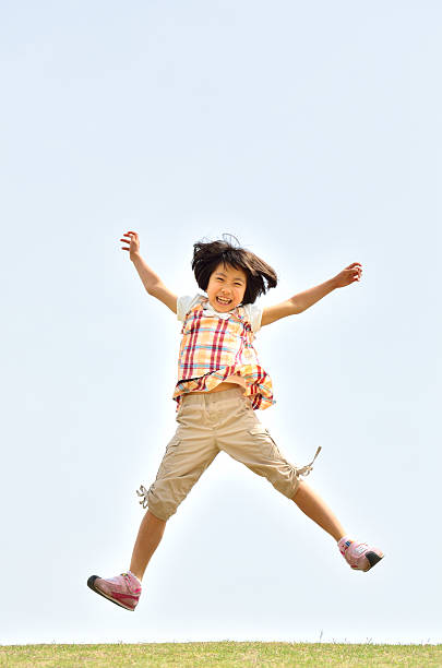 Happy laughing five year old boy jumping outdoors on trampoline, clear blue sky on sunny day