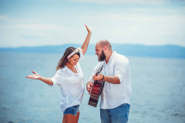 Young couple at the beach play guitar