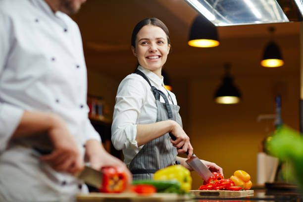 Cooking together Smiling trainee talking to expert while cutting raw pepper restaurant kitchen workers stock pictures, royalty-free photos & images