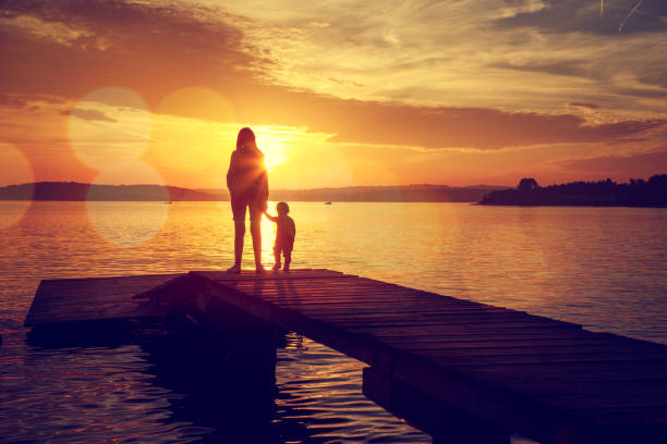 Silhouettes of Mother and Her Son by the Lake stock photo