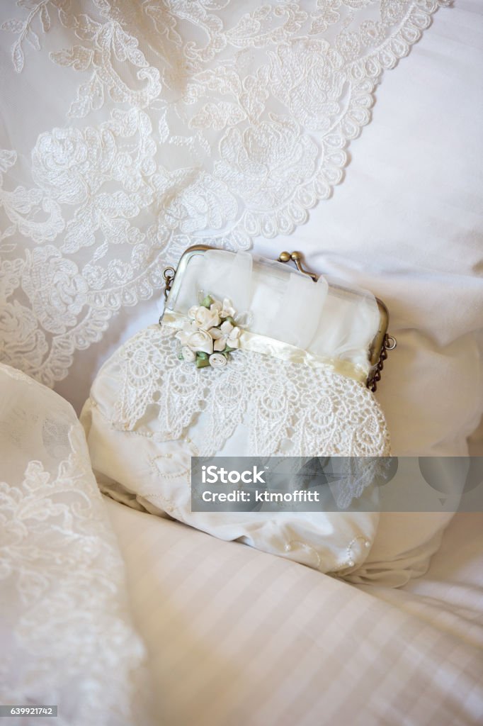 Vintage Purse Displayed On Bed with Wedding Dress Beautiful vintage clutch resting on a pillow with the edge of a wedding dress.  Lace - Textile Stock Photo