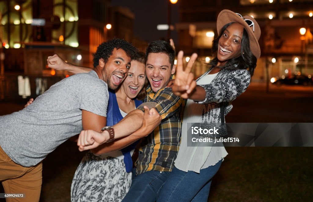 Multi-ethnic millenial group of friends taking a selfie photo Four young casual friends having fun taking pictures at an urban celebration with a cityscape view in the evening Friendship Stock Photo