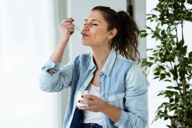 Photo of Beautiful young woman eating yogurt at home.