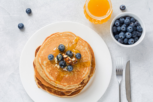 Stack of pancakes with fresh blueberries, nuts and honey on white plate. Healthy breakfast food.