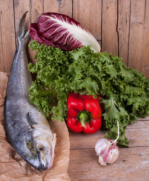 Lampuga Fish With Fresh Vegetables Raw lampuga fish with fresh lettuce, bell pepper, chicory and garlic, ingredients for a healthy mediterranean cuisine. lampuga stock pictures, royalty-free photos & images