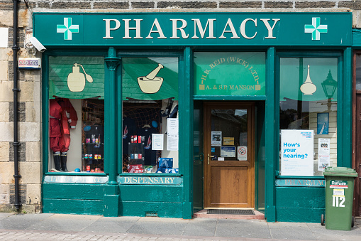 Wick, Scotland - June 4, 2012: Closeup of the green painted storefront of Wick Pharmacy owned by Mr. Manson. Display of colorful packages in windows. Trashcan upfront.