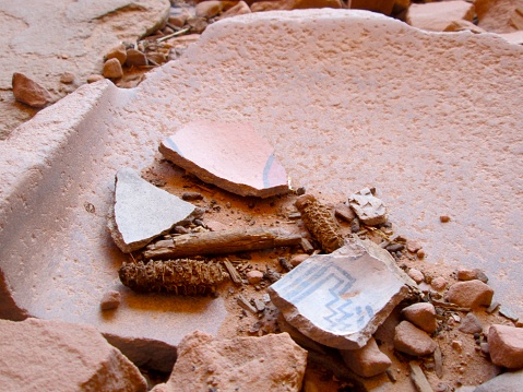 Prehistoric Native American artifacts, such as a corncob and pottery fragments, within a metate (ground stone tool).