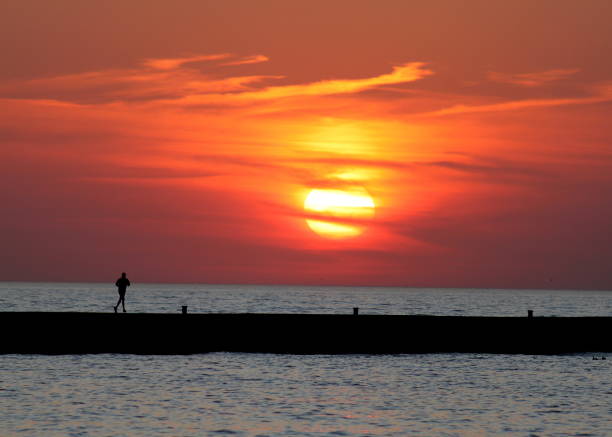 The silhouette of a runner was captured on a pier along lake Michigan at sunset.