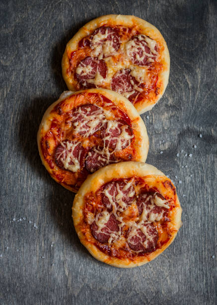 istock Mini salami pizza on a dark wooden background, top view 639960562