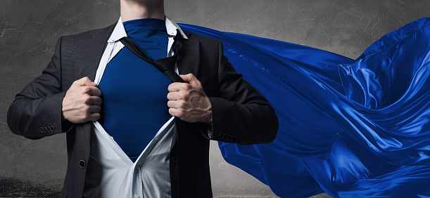 Young businessman dressed as superhero against concrete background