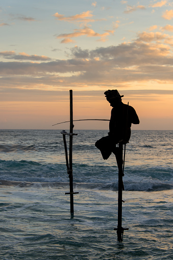Galle, Sri Lanka - January 21, 2017: Silhouette o a Sri Lankan stilt fisherman against a colorful sky during sunset.