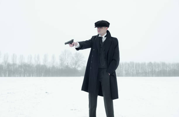 Retro 1920s english gangster with black coat and flat cap.