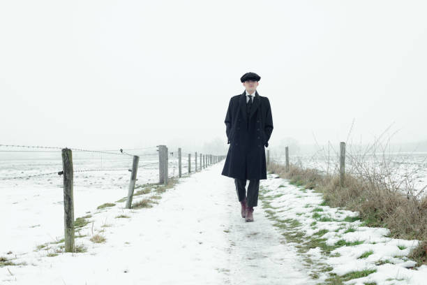 Retro 1920s english gangster with black coat and flat cap.