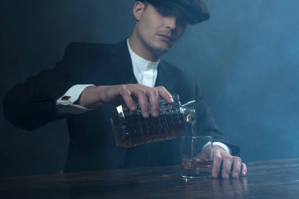 gangster inglese degli anni '20 con berretto piatto che versa whisky. - 20s businessman suit people foto e immagini stock