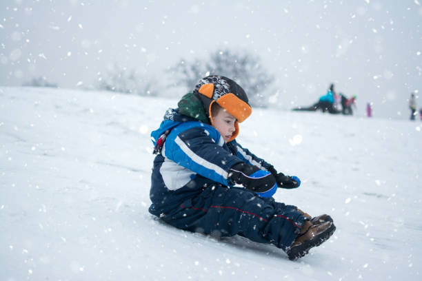 netter kleiner junge, der am verschneiten tag einen hügel hinunterschdelt. - little boys sled clothing slide stock-fotos und bilder