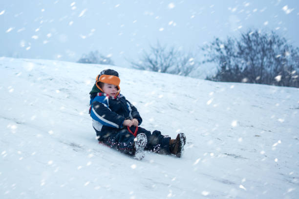 симпатичный маленький мальчик с тарелкой сани на открытом воздухе в зимний день. - little boys sled clothing slide стоковые фото и изображения