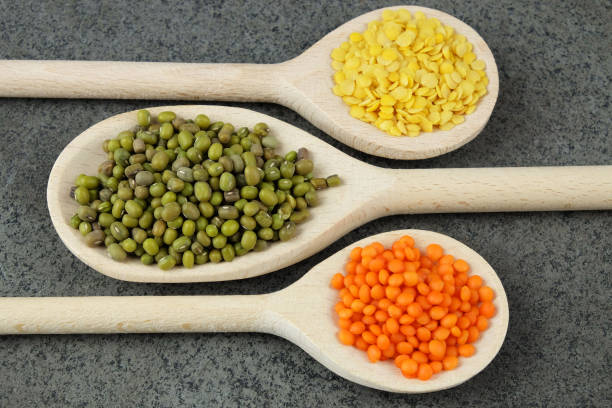 Three wooden spoons with green, yellow and red lentils.