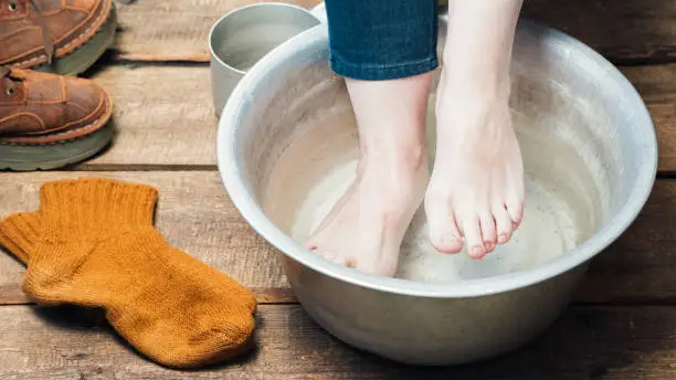 Footbath closeup. Bare feet in basin with warm water,  boots and wool socks on the floor