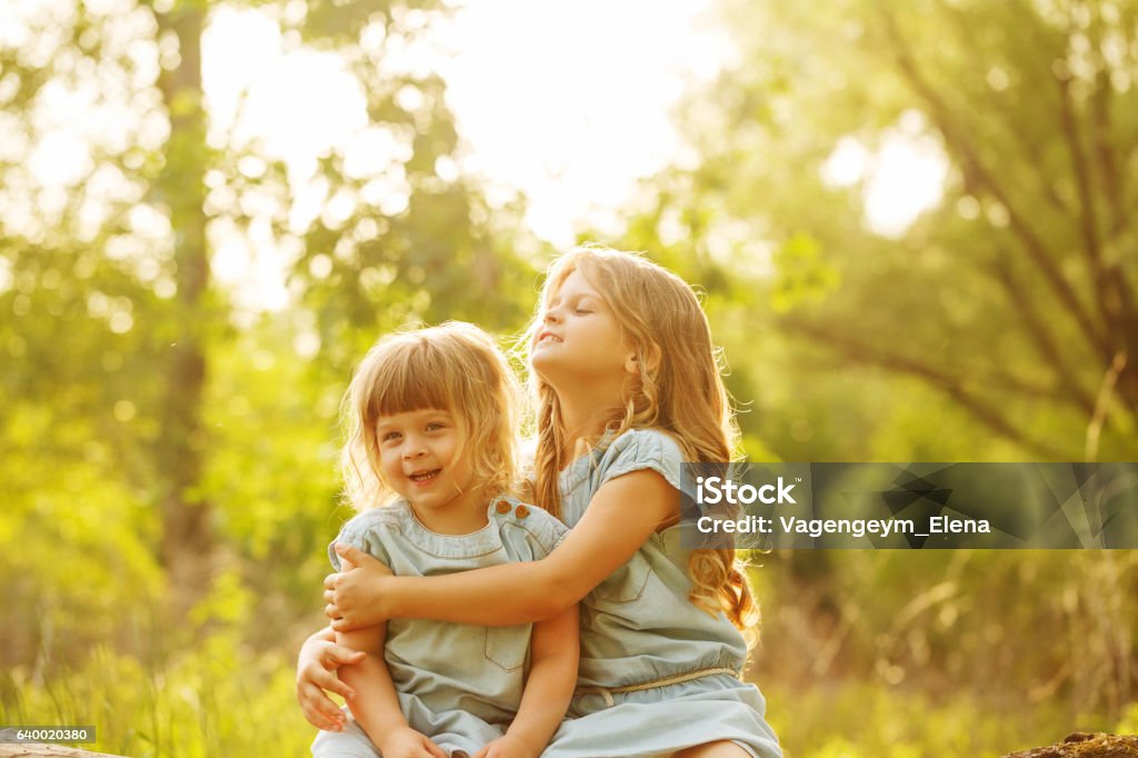 Two cute little sisters Two cute little sisters hugging in a park on a sunny summer day. Family time. Activity Stock Photo