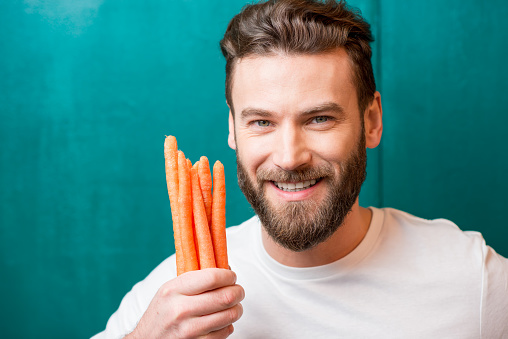 Close-up portrait of a handsome bearded man with mini carrots on the green background
