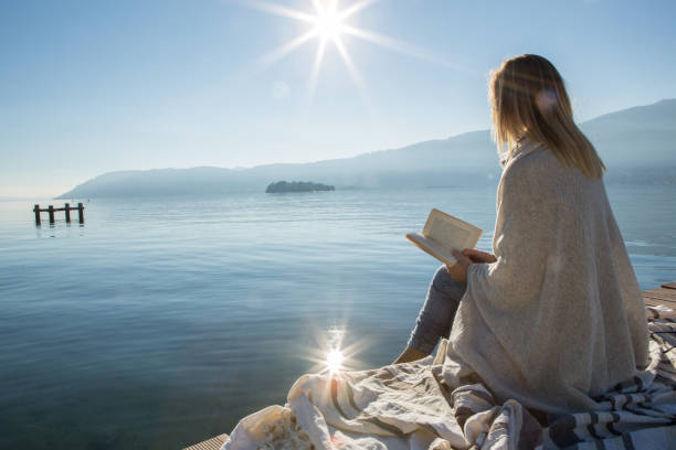 istock Young woman relaxing on lake pier with book 640025802