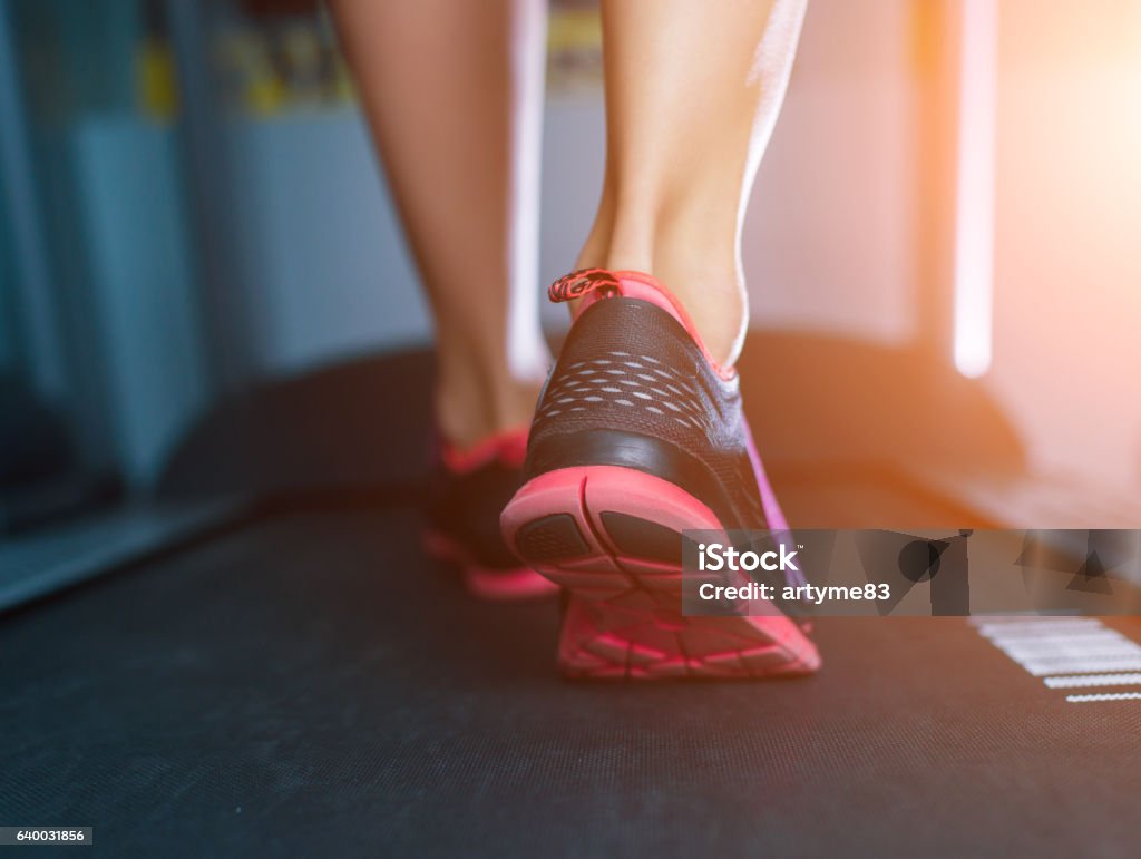 Female muscular feet in sneakers running on the treadmill. Female muscular feet in sneakers running on the treadmill at the gym. Concept for fitness, exercising and healthy lifestyle Treadmill Stock Photo