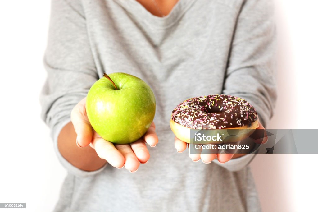 Dieting concept with woman choosing between healthy fruits and donut Dieting concept with young woman choosing between healthy fruits and sweets, holding green apple and tasty chocolate donut Candy Stock Photo