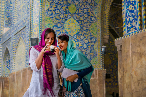 Young women are watching images at camera display, Isfahan, Iran Young female western tourist is showing her images on the camera display to her female iranian tourguide . Both are wearing the typcial simple headscarf (hijab or rousari) while they are visiting a mosque in Isfahan, iran. isfahan stock pictures, royalty-free photos & images