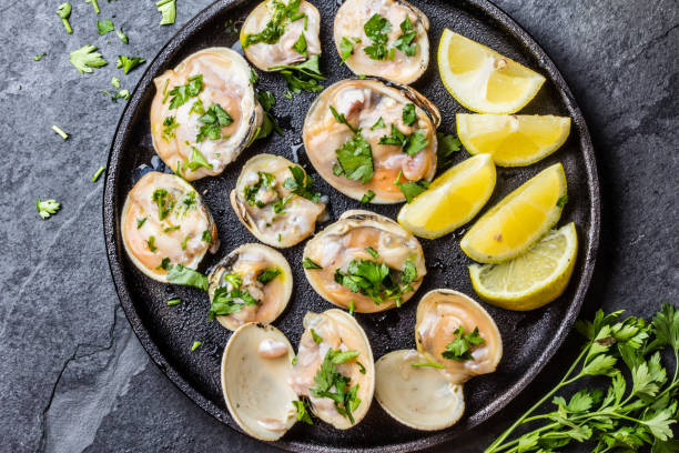 istock Raw clams with lemon, herbs on black iron plate 640042760