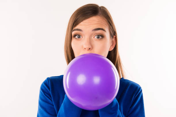 istock cute smiling young woman blowing violet balloon 640051750