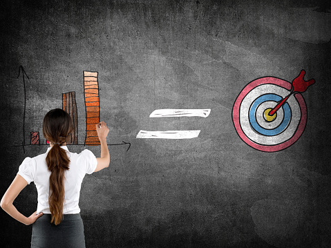 Businesswoman writing on blackboard with bar graph and dartboard icon