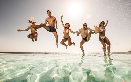 Low angle view of happy people having fun in summer day while jumping into the swimming pool.