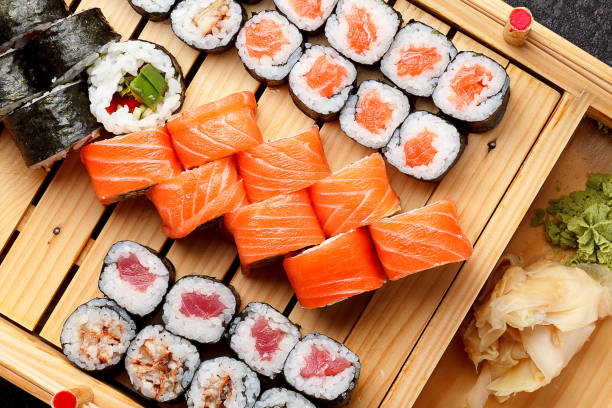 sushi incastonato su un piatto di legno e sfondo di cemento scuro. - sushi foto e immagini stock