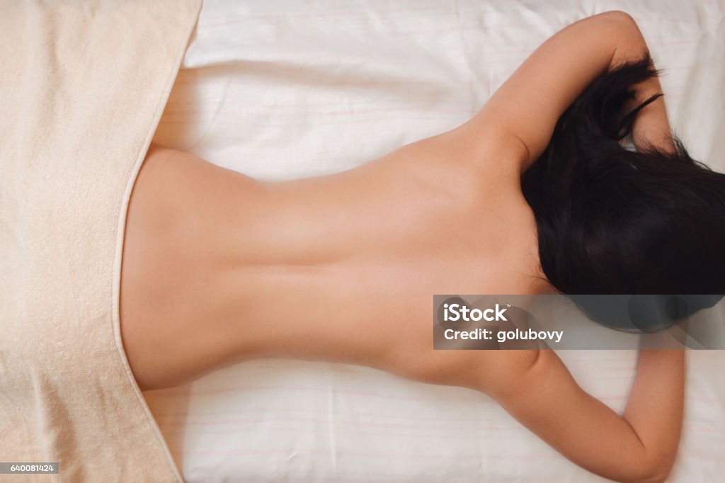 Nude woman back on massage table flat lay Nude woman back on massage table flat lay. Top view on half naked brunette with perfect body lying on her stomach at spa salon. Beauty, slim, health care, pleasure, fitness, thin waist concept Back Stock Photo