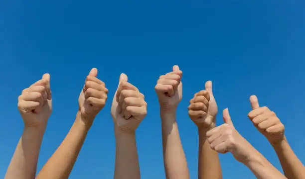 Group of hands giving thumbs up over blue sky