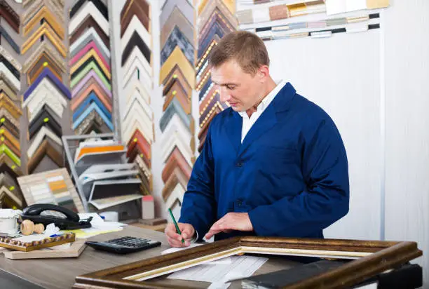 portrait of glad american man seller working with picture frames in atelier