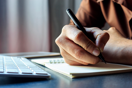close up of hand businessman working with writing on notebook, computer and tablet at workplace. film colors tone, soft-focus and over light in the background