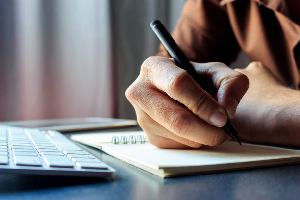 Writing down your goals can make them feel more tangible. businessman close up of hand businessman mid term financial goals long term financial goals working with writing on notebook, computer and tablet at workplace. film colors tone, soft-focus and over light in the background write down stock pictures, royalty-free photos & images
