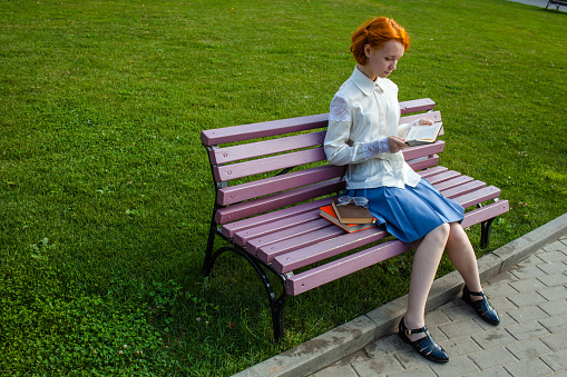 Girl outdoors sitting on a bench reading a book