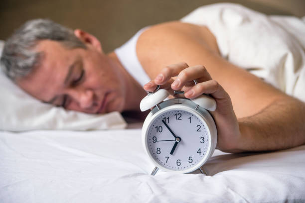 istock Man lying in bed turning off an alarm clock 640097060