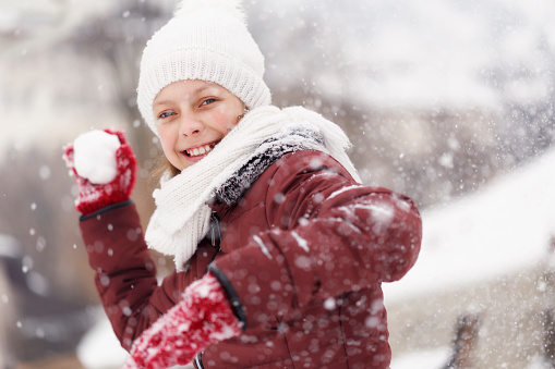 Smiling teenage girl throwing snowball - winter acitivities